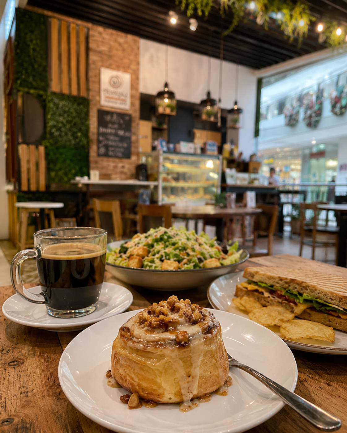 Annipie Abreeza interior with cinnamon roll, salad, sandwich and coffee on a wooden table
